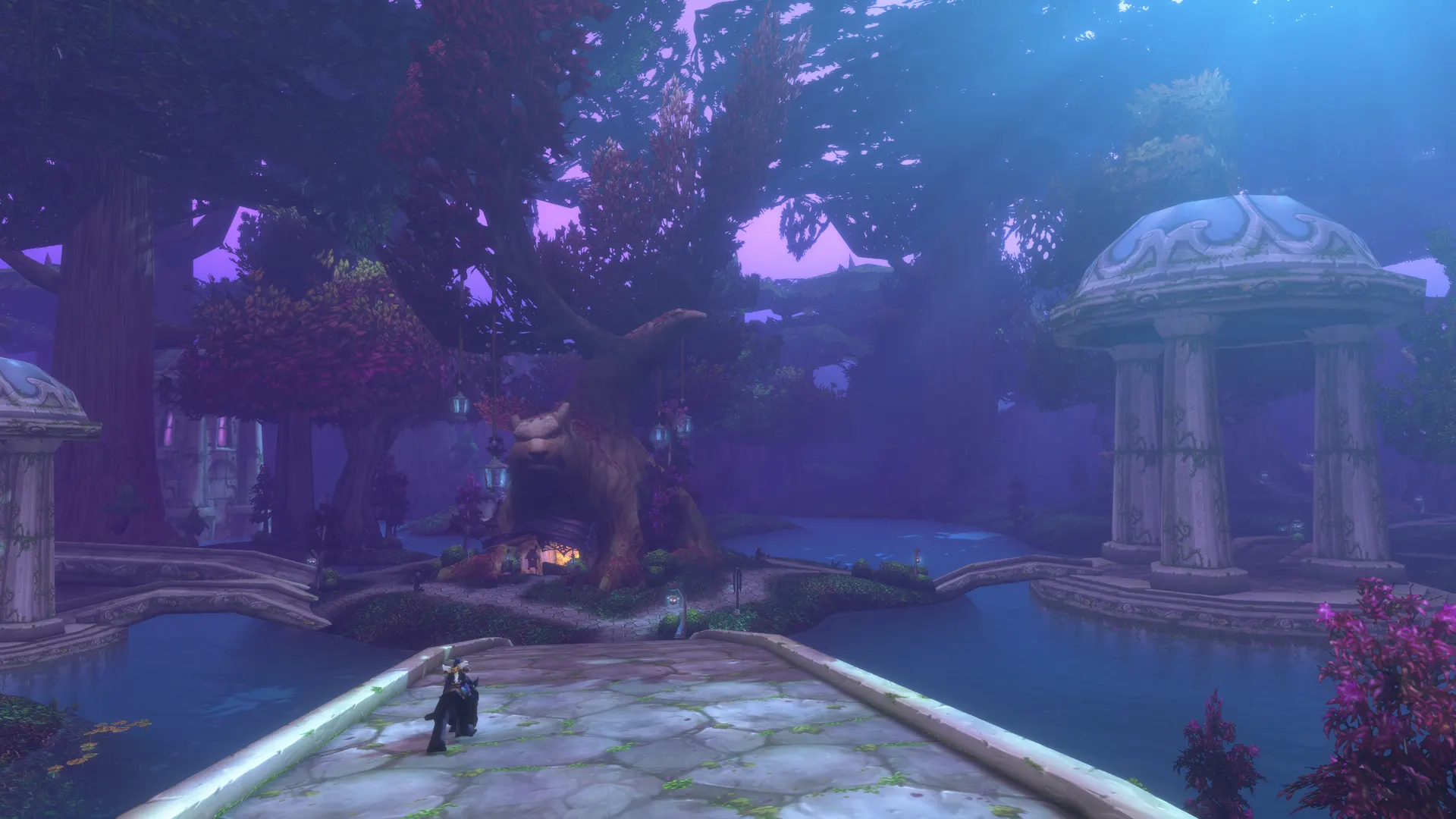 A lone mounted character on a stone bridge in Darnassus, with a large tree-carved building and a domed pavilion under purple evening light